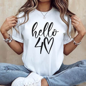 May include: White t-shirt with the words "hello 40" in black script and a heart symbol. The shirt is a casual style, suitable for everyday wear.