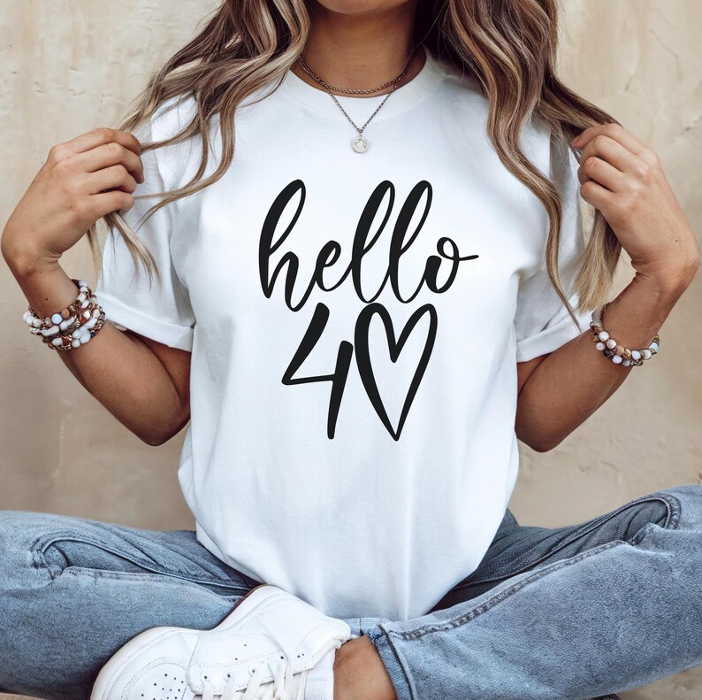 May include: White t-shirt with the words "hello 40" in black script and a heart symbol. The shirt is a casual style, suitable for everyday wear.