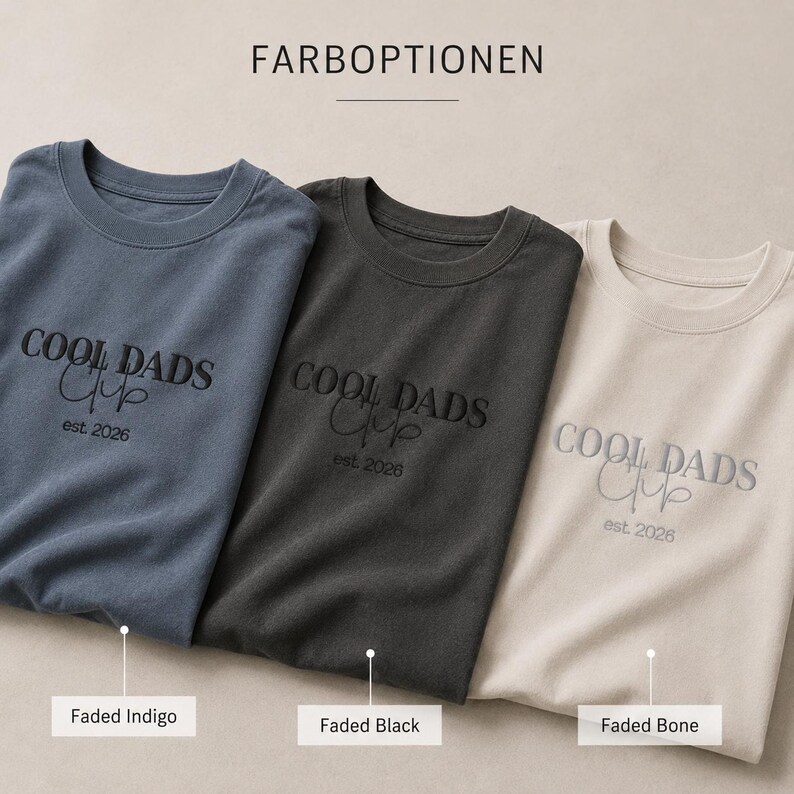 May include: Three crewneck t-shirts in faded indigo, faded black, and faded bone colors. Each shirt features the embroidered text "COOL DADS Club" and "est. 2026" in a contrasting thread. The image includes the German text "FARBOPTIONEN" above.