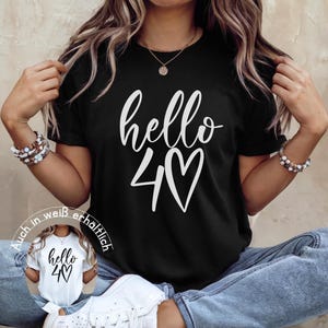 May include: Black t-shirt with the words "hello 40" in white script and a heart symbol. The shirt is a crew neck style. A smaller image of the same shirt in white is in the lower left corner.