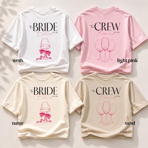 May include: Four short-sleeve t-shirts in white, light pink, natural, and sand colors. Each shirt features a graphic print with text reading The BRIDE or The CREW, along with EST. 2026, a name, and a line drawing of either one or three wine glasses.