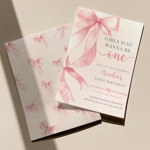 Puede incluir: Dos tarjetas de invitación rectangulares con un diseño de lazos rosas en acuarela. La tarjeta frontal muestra el texto GIRLS JUST WANNA BE one, JOIN US TO CELEBRATE Amelia's FIRST BIRTHDAY, SATURDAY 25 NOVEMBER y detalles del evento.