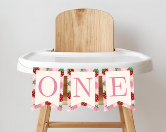 Puede incluir: Una pancarta con la palabra "ONE" en letras rosas, decorada con fresas y flores, cuelga de una trona. La pancarta está diseñada para una celebración de primer cumpleaños.
