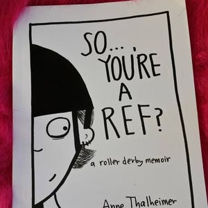 May include: A black and white book cover with the title "SO... YOU'RE A REF?" and the subtitle "a roller derby memoir." The cover features a cartoon illustration of a person with a referee uniform. The author's name is Anne Thalheimer aka Anne Persand.