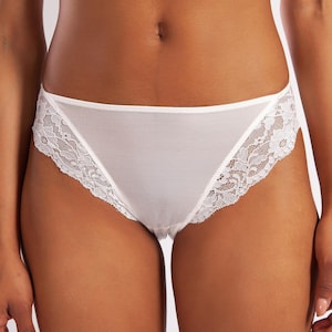 Puede incluir: Bragas blancas con delicados bordes de encaje. La ropa interior tiene un corte clásico y está hecha de una tela suave y opaca. El encaje añade un toque de elegancia al diseño.
