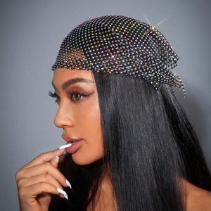 Puede incluir: Un pañuelo negro cubierto de pequeños y brillantes pedrería. El cubrecabezas está drapeado sobre la cabeza y el cabello. El pañuelo es un accesorio de moda.