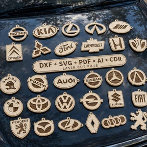 Puede incluir: Una colección de logotipos y emblemas de marcas de coches de madera clara cortados con láser, incluyendo Datsun, Kia, Ford, Chevrolet, Honda, Skoda, Volvo, Audi, Nissan, BMW, Toyota, VW, Opel, Suzuki, Fiat, Peugeot, Mazda y Renault, con un letrero central que dice DXF SVG PDF AI CDR LASER CUT FILES.