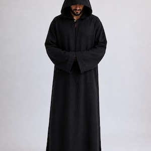 May include: A floor-length black hooded robe with long sleeves and a single button closure at the neckline. The garment features a pointed hood, wide cuffs, and side slits at the hem, providing a loose and straight silhouette in a solid black fabric.