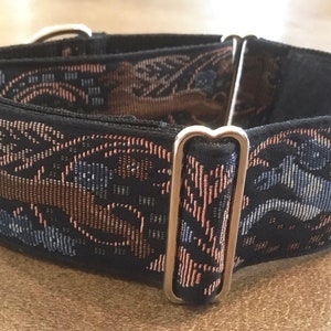 Puede incluir: Un collar negro para perros con un patr&oacute;n decorativo tejido en tonos marr&oacute;n, azul y rosa. El collar presenta herrajes met&aacute;licos plateados. El patr&oacute;n tiene un dise&ntilde;o floral y geom&eacute;trico.