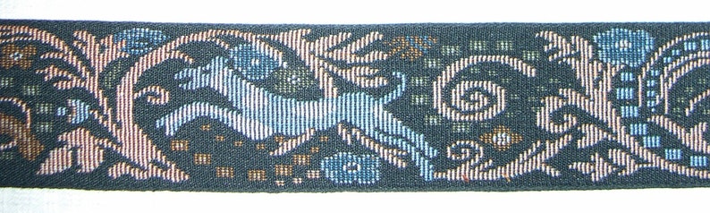 Puede incluir: Cinta tejida con un patr&oacute;n repetitivo de un animal azul claro, posiblemente un ciervo, entre elementos florales y foliares estilizados. El fondo es de color verde azulado oscuro, con acentos marrones y blancos.