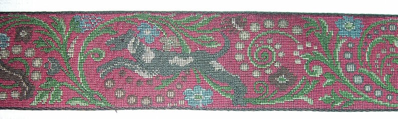 Puede incluir: Cinta tejida con un fondo burdeos y un patr&oacute;n repetido de animales estilizados, flores y follaje. El dise&ntilde;o incorpora tonos verdes, azules y marrones, creando una apariencia detallada y texturizada. Los bordes de la cinta est&aacute;n acabados con un borde oscuro.