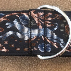 Puede incluir: Un collar negro para perros con un patr&oacute;n decorativo que presenta un caballo corriendo y elementos florales en tonos azules, beige y blanco. El collar tiene un anillo en D de metal plateado y herrajes ajustables.