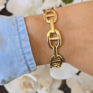 May include: A white ceramic mug with a black handle and the text "But First, Coffee" in a bold, black font. The mug is set against a blurred background, suggesting a cozy setting.