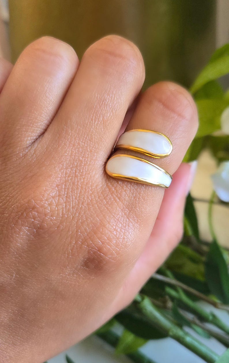 Puede incluir: Un anillo dorado con un dise&ntilde;o de esmalte blanco. El anillo se envuelve alrededor del dedo con dos secciones superpuestas en forma de l&aacute;grima. El dise&ntilde;o del anillo es simple y elegante, adecuado para el uso diario.
