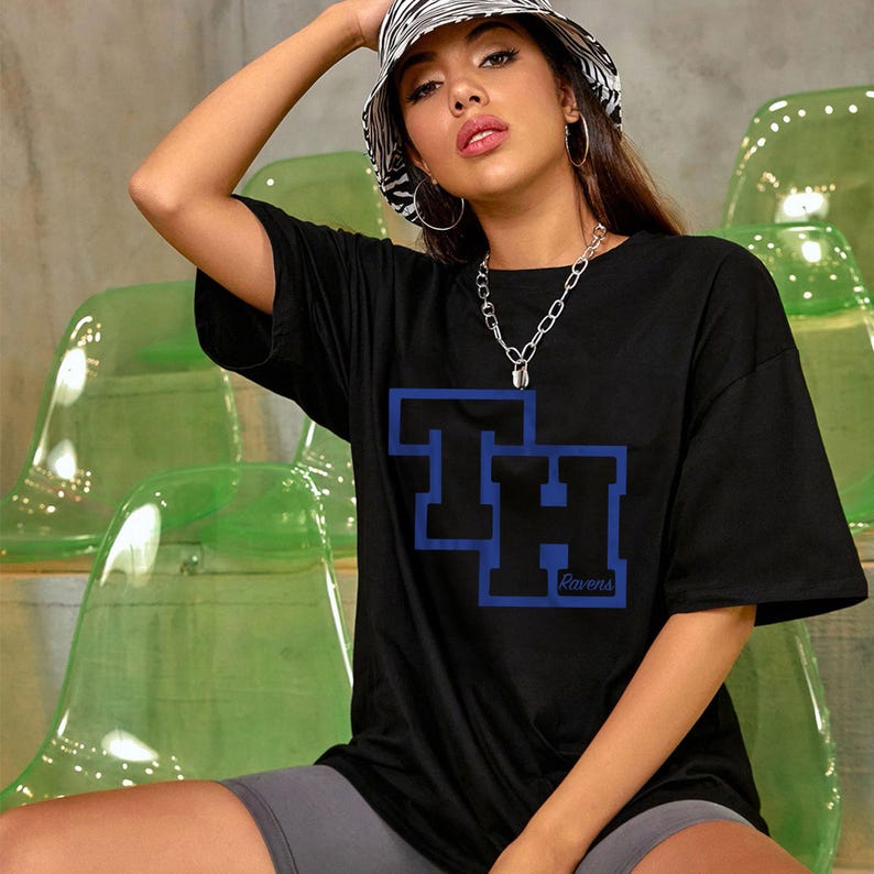 Peut inclure: T-shirt noir avec un motif bleu et noir "TH Ravens". Le haut est port&eacute; avec un chapeau seau z&eacute;br&eacute; et un collier cha&icirc;ne argent&eacute;. Le t-shirt est de style d&eacute;contract&eacute;.