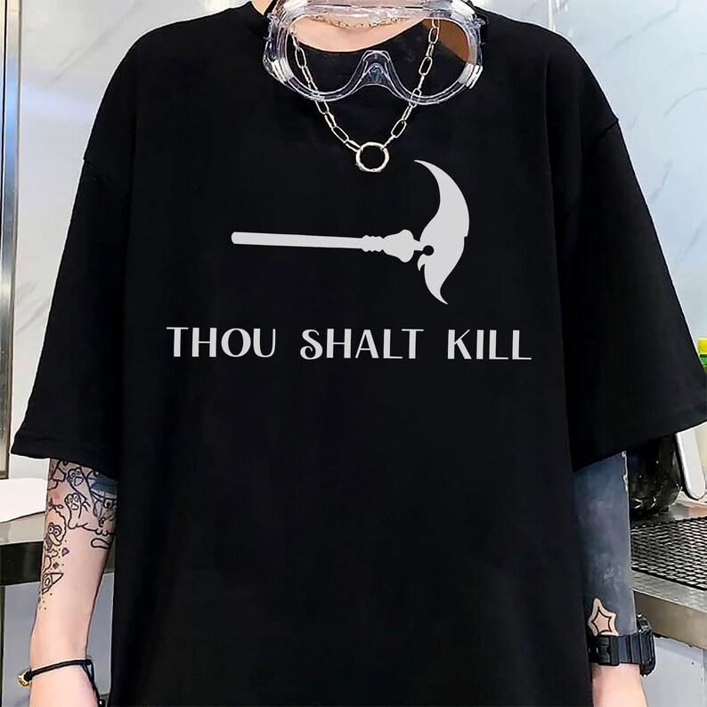 May include: Black t-shirt with a white graphic of a scythe and the text "THOU SHALT KILL". The shirt has short sleeves and a relaxed fit. A pair of clear safety glasses and a necklace are worn.