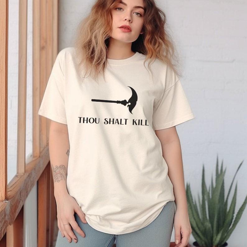 May include: Cream-colored t-shirt with a black graphic of a scythe and the text "THOU SHALT KILL". The short-sleeved shirt is made of a soft material and has a relaxed fit. The shirt is a casual wear item.