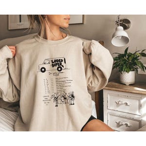 May include: Beige sweatshirt with a black and white graphic of a van and band. Text on the sweatshirt reads "Loded Diper Tour" with a list of tour dates and "Leave the rocking to us."