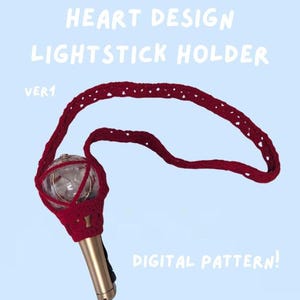 May include: A red crocheted lightstick holder with a heart design, featuring a strap and a gold-coloured base. The text "HEART DESIGN LIGHTSTICK HOLDER" and "DIGITAL PATTERN!" are visible on a light blue background.