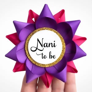 May include: Purple and pink bow with a gold glitter circle that says "Nani to be" in black text.
