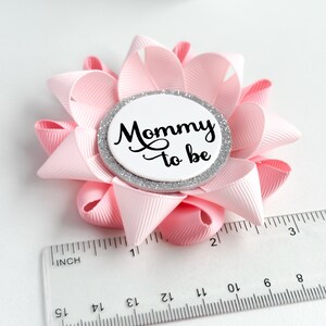 May include: Pink and silver mommy-to-be button with a white circle and black text. The button is about 2 inches in diameter.