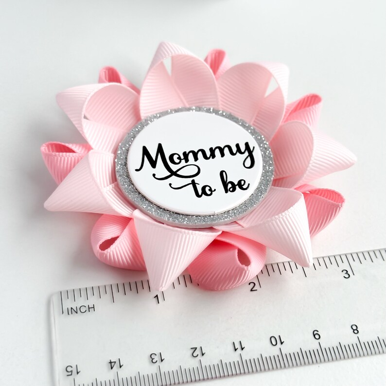 May include: Pink and silver mommy-to-be button with a white circle and black text. The button is about 2 inches in diameter.