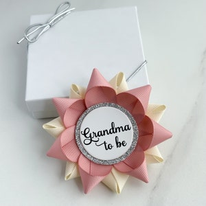 May include: A pink and cream bow with a silver glitter circle that says "Grandma to be" in black script.