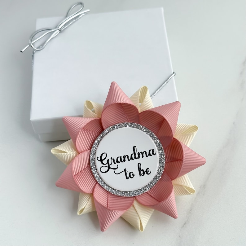 May include: A pink and cream bow with a silver glitter circle that says "Grandma to be" in black script.