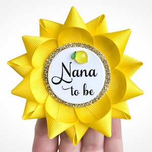 May include: Yellow and white 'Nana to be' button with a small lemon design. The button is attached to a yellow bow.