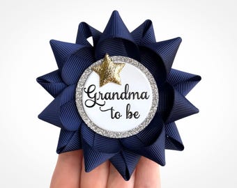 May include: A navy blue bow with a white circle in the center. The circle has a gold star and the text "Grandma to be" in black.