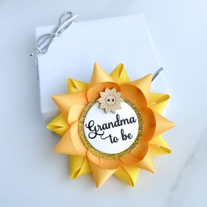 May include: Yellow and gold bow with a white circle that says "Grandma to be" and a small wooden button in the center.