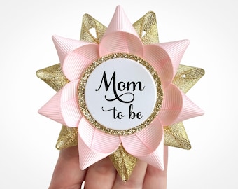 Könnte beinhalten: Rosa-goldener Sternförmiger Anstecker mit einem weißen Kreis in der Mitte, auf dem "Mom to be" steht.