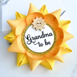 May include: Yellow and gold bow with a white circle that says "Grandma to be" and a small wooden sunflower with a button in the center.