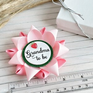May include: Pink and green bow with a white circle that says "Grandma to be" and a red strawberry on top. The bow is about 3 inches in diameter.