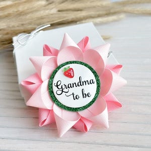 May include: Pink and green grandma to be button with a strawberry design.
