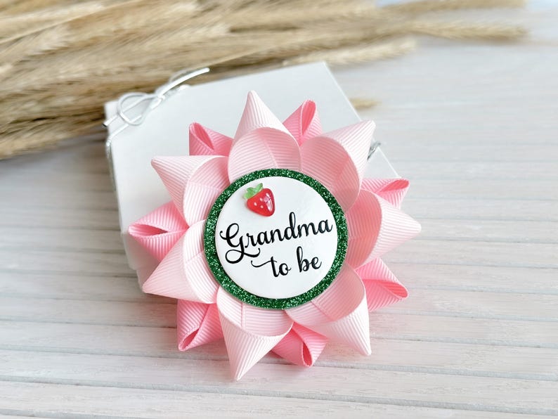 May include: Pink and green grandma to be button with a strawberry design.