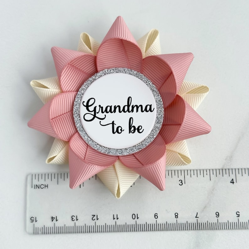 May include: A pink and ivory bow with a silver glitter circle that says "Grandma to be" in black script.