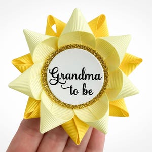 Baby shower pin made of light yellow and yellow ribbon in the shape of a flower with gold accent and custom text: Grandma to be