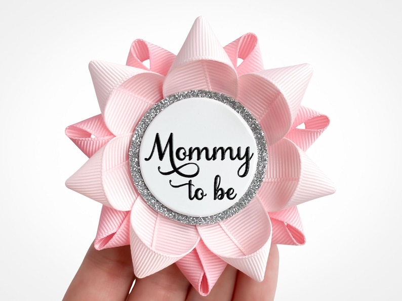 A baby shower corsage made of pale pink and pink ribbon with silver accent and text: Mommy to be