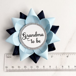 May include: A light blue and navy blue bow with a white circle in the centre that says "Grandma to be" in black lettering. The circle has a silver glitter border.