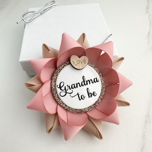 May include: A pink and beige bow with a white circle that says "Grandma to be" and a small wooden heart that says "Love".