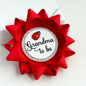 May include: Red and white grandma-to-be button with a ladybug design. The button has a silver glitter border.