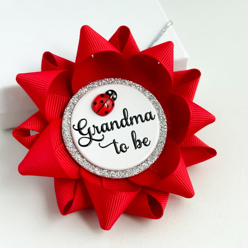 May include: Red and white grandma-to-be button with a ladybug design. The button has a silver glitter border.