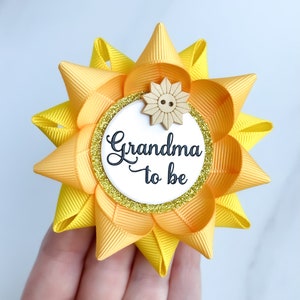 May include: Yellow and orange bow with a white circle that says "Grandma to be" and a small wooden sunflower with a button in the center.