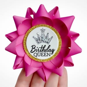 Flower pin made of magenta ribbon with gold accent and silver crown decoration. Custom text: Birthday Queen