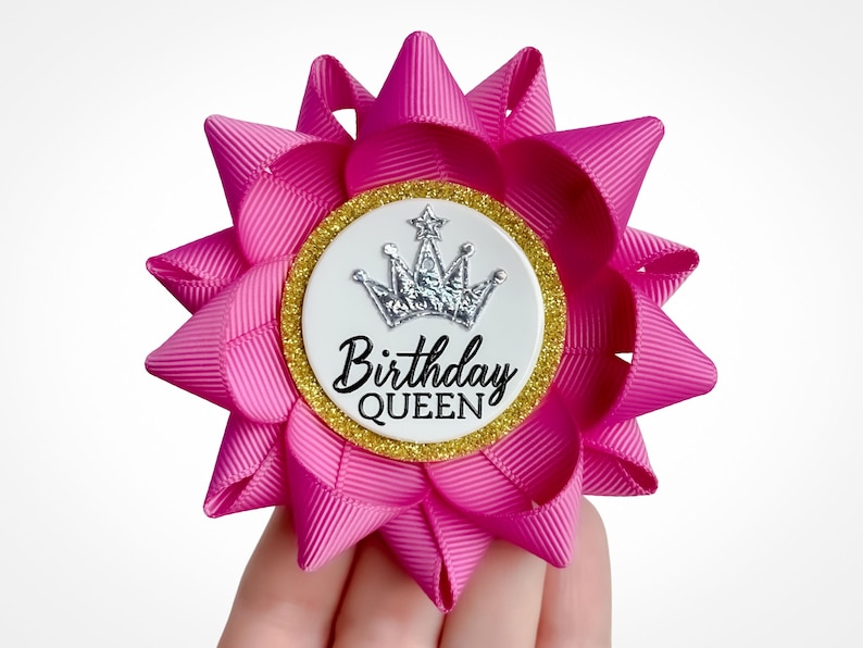 Flower pin made of magenta ribbon with gold accent and silver crown decoration. Custom text: Birthday Queen