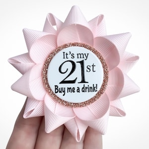 May include: A pink and gold glitter 21st birthday button with the text "It's my 21st Buy me a drink!"