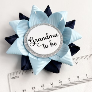 May include: A light blue and navy blue bow with a silver glitter circle that says "Grandma to be" in black script.