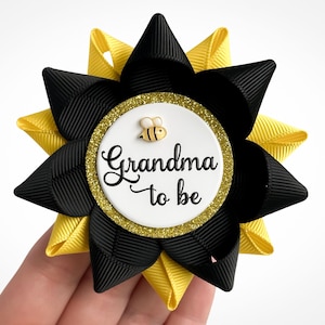 May include: Black and yellow bee-themed grandma-to-be button with a white circle and gold glitter. The button says "Grandma to be" with a small bee illustration.
