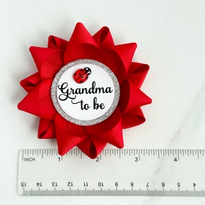 May include: Red and white grandma to be button with a ladybug on it. The button is about 2 inches in diameter.